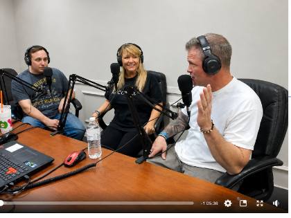 Three people wearing headphones sitting at a table during a podcast recording session
